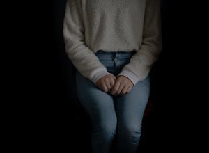 Crop unrecognizable woman sitting with hands on laps in darkness