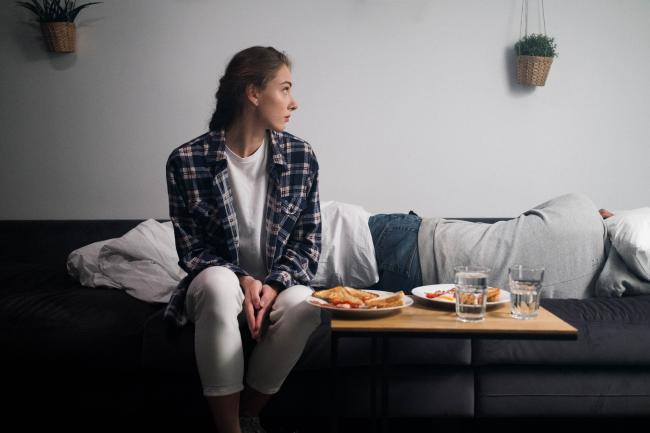 Woman in Blue and White Plaid Dress Shirt Sitting on Bed Beside the Side Table with Food